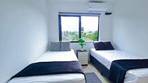 Een slaapkamer met twee bedden, een raam, een potplant en een klein nachtkastje.