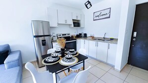 A compact kitchen with white cabinets, a built-in microwave, and a dining table set with black and white plates. - Very cozy apartment, ideal for couples or families. (San Salvador)