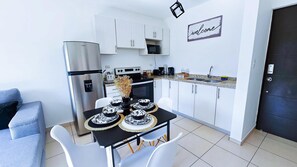 A compact kitchen with white cabinets, a built-in microwave, and a dining table set with black and white plates. - Very cozy apartment, ideal for couples or families. (San Salvador)