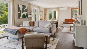 Una sala moderna con un sofá seccional, una mesita, un mueble para televisión y vistas al exterior con zonas verdes.