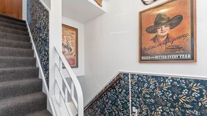 Una escalera con barandilla blanca, un papel tapiz con estampado floral y un cartel antiguo.