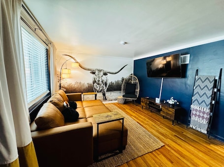 A modern living room with a large sofa, a mounted TV, a decorative wall piece, and a unique chair.. The Longhorn Hideout