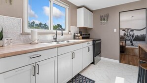 Una cocina moderna con un amplio ventanal, armarios blancos y un lavavajillas negro.
