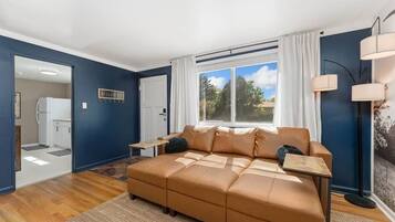 Ein Wohnzimmer mit einer Couch, einem kleinen Tisch, einer Lampe und einem Fenster mit Vorhängen.