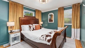 Un dormitorio con una cama de madera, una mesita de noche, un espejo y una ventana con cortinas.