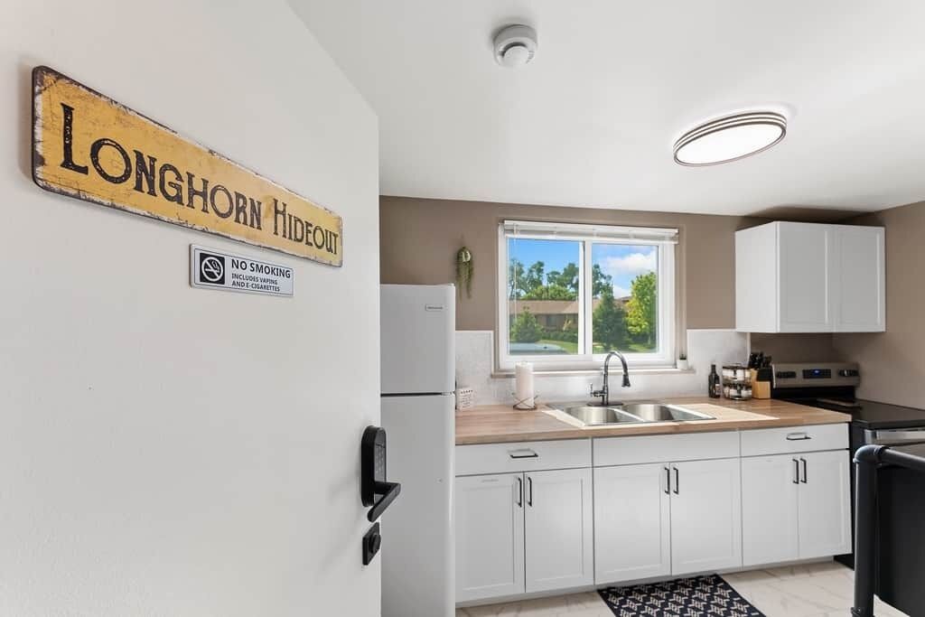 A modern kitchen with white cabinets, a sink, and a window with a view of greenery.
