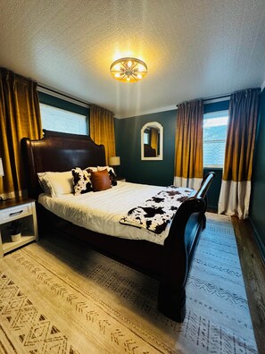 A bedroom with a wooden bed, a nightstand, a mirror, and a ceiling light fixture.