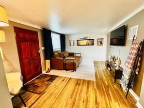 A living room with a sofa, a television, and a door. - The Wildflower Hideout (Cheyenne)