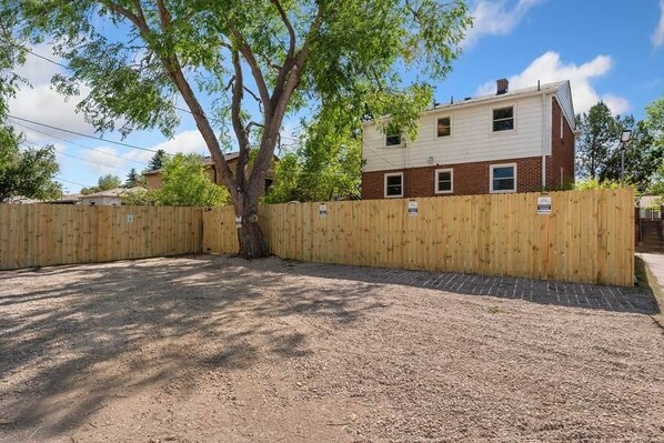 A fenced outdoor area with a tree and a two-story building in the background.
