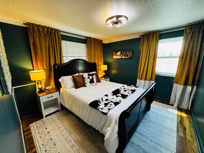 Een hotelkamer met een bed, nachtkastjes, een lamp, een plafondventilator en een raam met gordijnen.