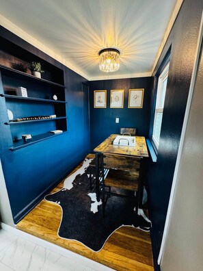 Een kleine, knusse kamer met een donkerblauwe wand, een houten tafel, een vachttapijt en een kroonluchter.