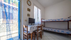 Una habitación con una cama litera, un escritorio con computadora, sillas, una ventana con cortinas y un reloj de pared.