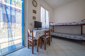 Una habitación con una cama litera, un escritorio con computadora, sillas, una ventana con cortinas y un reloj de pared.