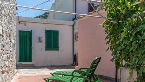 Un patio con un muro de piedra, un edificio con contraventanas verdes y un banco.