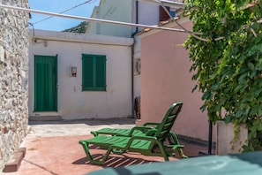 Un patio con un muro de piedra, un edificio con contraventanas verdes y un banco.