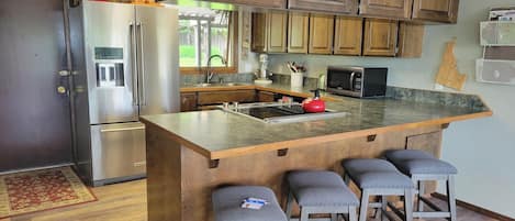A kitchen with wooden cabinets, a stainless steel refrigerator, a microwave, and a granite countertop.