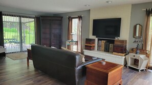 Uma sala de estar com sofá, televisão fixada em parede de tijolos, lareira com espaço para guardar objetos e porta de vidro deslizante que dá para uma área externa.