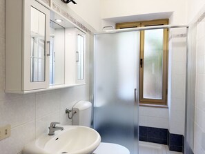 Een badkamer met een wit wastafelmeubel, een spiegel en een douche met ruitverdelende glazen deuren.