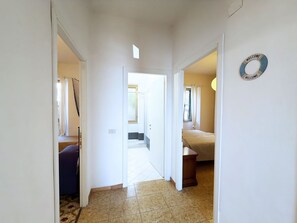 Een gang die leidt naar een slaapkamer met een bed en nachtkastje.