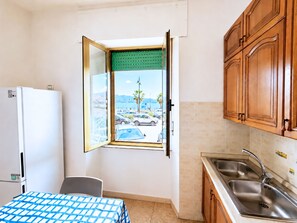 A compact kitchen with a view of parked cars and palm trees outside. - Le Finestre sul Porto (Portoferraio)