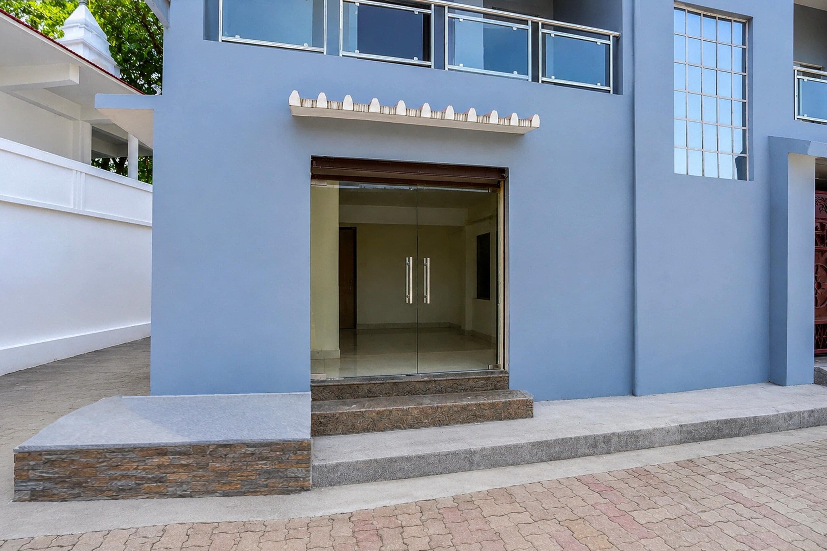 A modern building with a blue facade, a glass entrance, and a set of steps leading to the door.