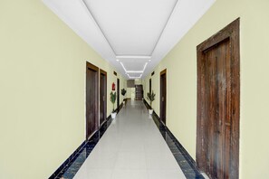 Un pasillo largo y estrecho con suelo de baldosas, puertas de madera a ambos lados y una escalera al final.
