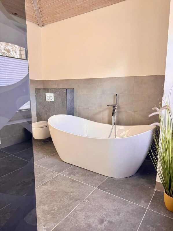 Ein modernes Badezimmer mit freistehender Badewanne, Toilette und einem Topf mit Pflanze.