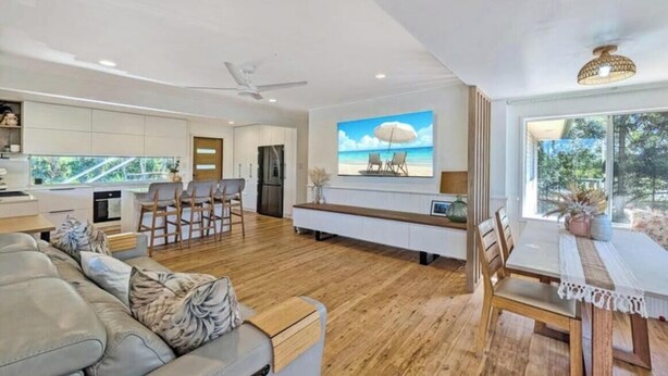 A modern kitchen with white cabinets, a dining area with a white table and chairs, and a large window with a view of greenery. - Spacious Family Retreat with Pool, Waterslide & Dual Living Minutes from Beaches (Kuluin)
