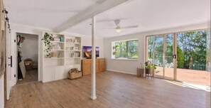 A spacious room with a wooden floor, a bookshelf, a ceiling fan, and large windows. - Spacious Family Retreat with Pool, Waterslide & Dual Living Minutes from Beaches (Kuluin)