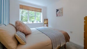 Ein Schlafzimmer mit Bett, Fenster, Nachttisch und einem Wandbild.