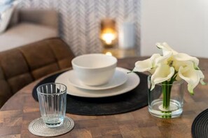 Una mesa de comedor con un bol blanco, un vaso transparente y un jarrón con flores blancas.