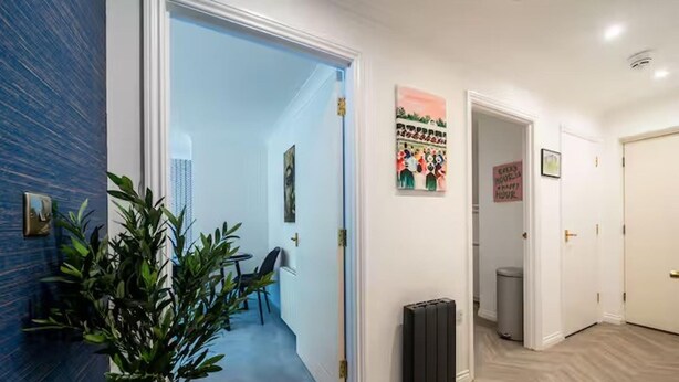 Ein Flur mit blauer Wand, einer Pflanze, einer zurueckfuehrenden Tür zu einem Zimmer und einem Poster an der Wand.