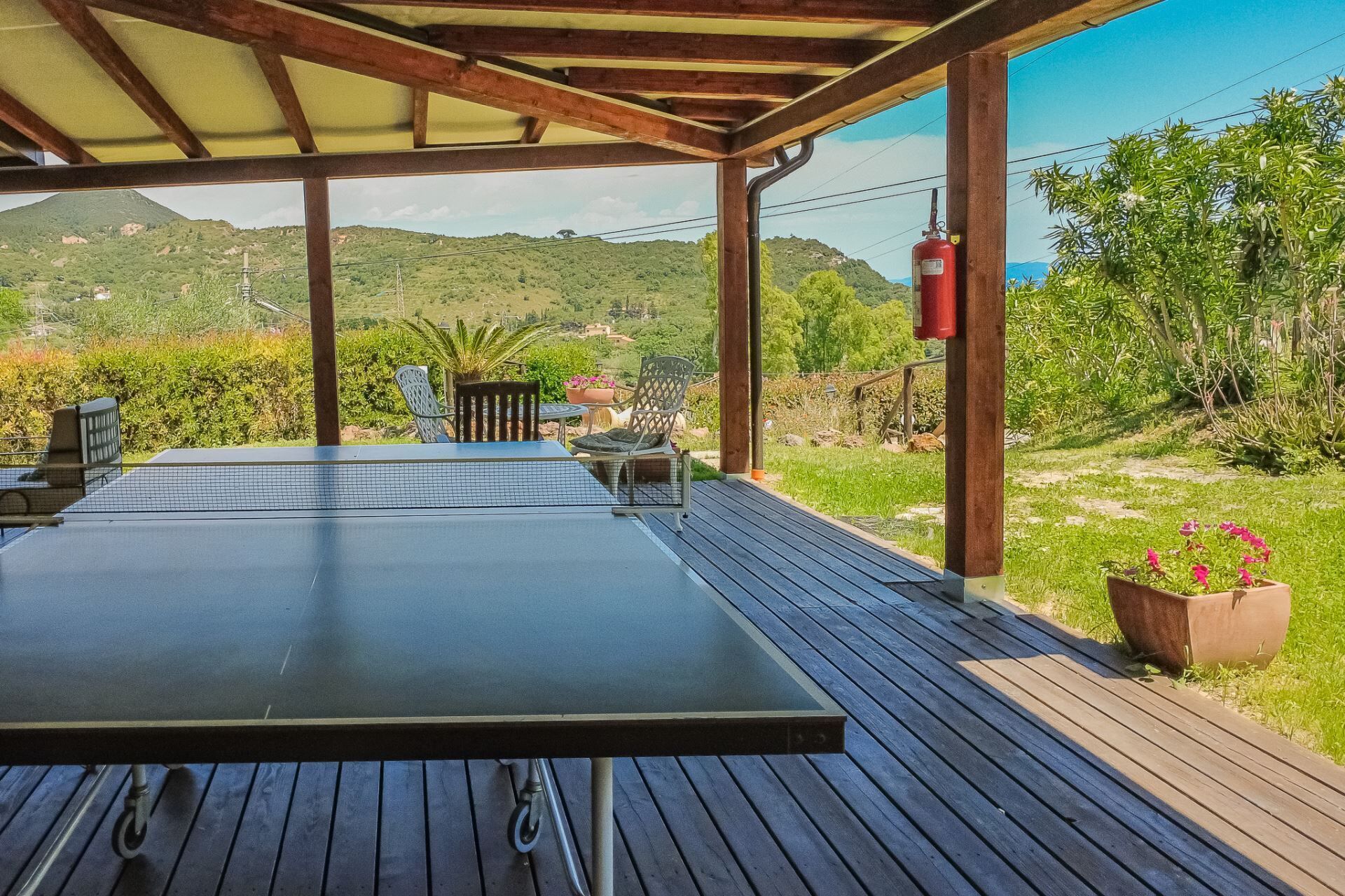 Un espacio al aire libre cubierto con una mesa y sillas, un extintor y vistas a un paisaje verde.