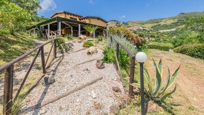 A building with a covered patio area, a gravel pathway leading to it, and a view of a hilly landscape in the background. - Tra Cielo e Mare - Rooms Rio Marina - Tra Cielo e Mare - Curcuma (Rio Marina)