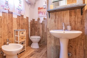 A bathroom with wooden walls, a white sink, a toilet, and a bidet. - Tra Cielo e Mare - Rooms Rio Marina - Tra Cielo e Mare – Paprika (Rio Marina)