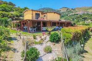 A yellow building with a covered patio, outdoor seating, and a garden path leading to the entrance. - Tra Cielo e Mare - Rooms Rio Marina - Tra Cielo e Mare – Paprika (Rio Marina)