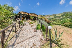 A building with a covered patio area, a gravel pathway leading to it, and a view of a hilly landscape in the background. - Tra Cielo e Mare - Rooms Rio Marina - Tra Cielo e Mare – Paprika (Rio Marina)