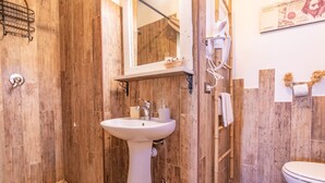 Kylpyhuone, jossa on puuseinä, pesuallas, peili, suihku ja wc.