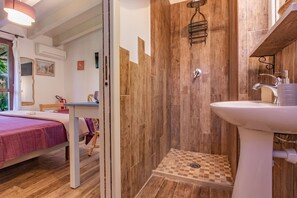 Ein Zimmer mit einem Bett, einer Dusche mit Holzwänden, einem Waschbecken und einem Fenster mit Blick.