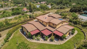Una grande casa a più piani con tetto in tegole, immersa nel verde e circondata da colline.