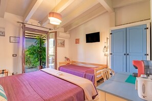 Ein Zimmer mit zwei Betten, einem Fernseher, einer Kaffeemaschine und Blick auf Grünflächen.