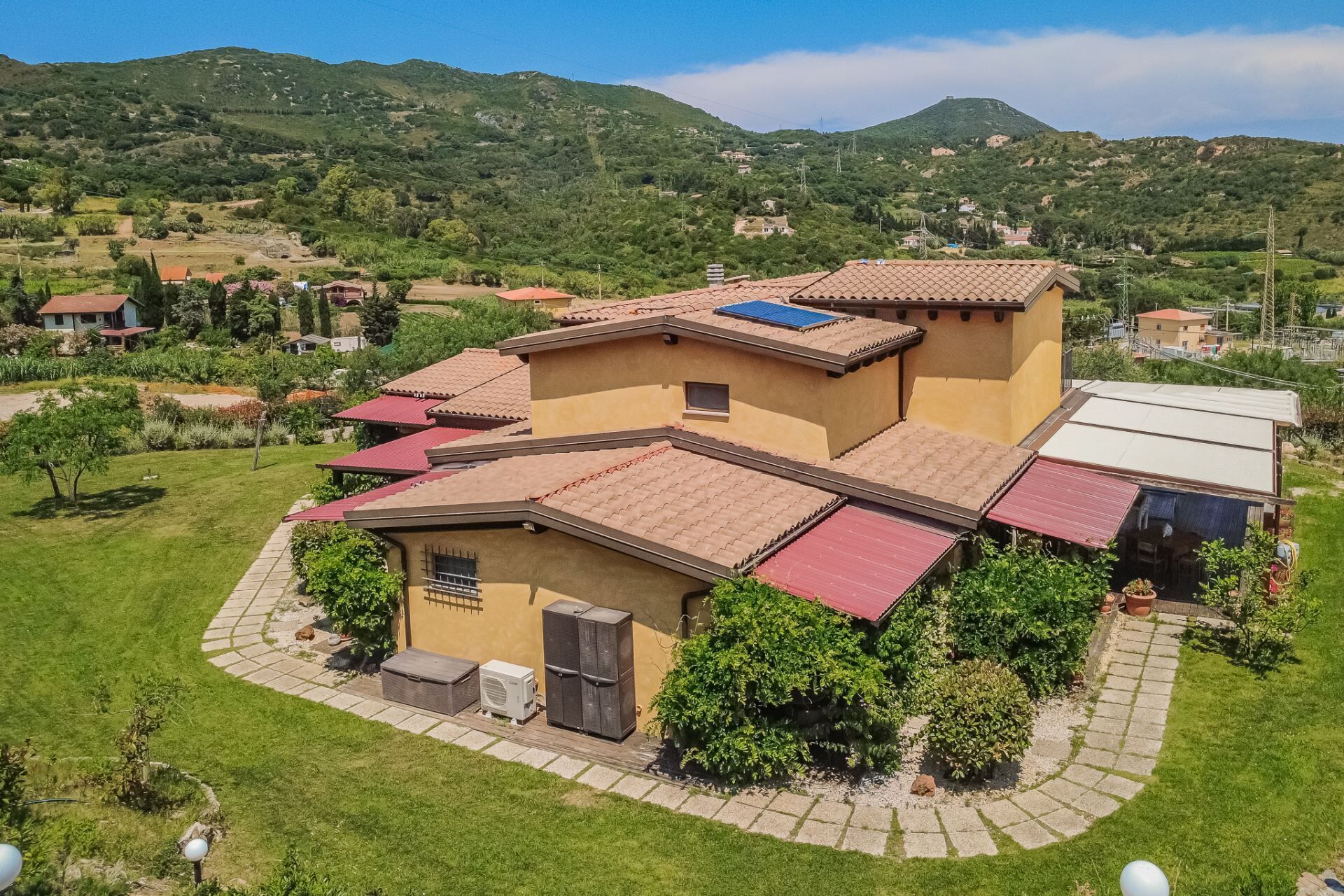 A residential building with multiple red-tiled roofs, a central courtyard, and a surrounding green landscape.