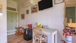 Ein Zimmer mit Schreibtisch, Stuhl, Klimaanlage, Fernseher, gerahmten Bildern und einem Feuerlöscher.