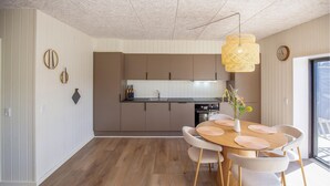 A modern kitchen with a central island, a dining area with a round table and chairs, and a hanging light fixture. - Lovely home in Hvide Sande with sauna (Hvide Sande)