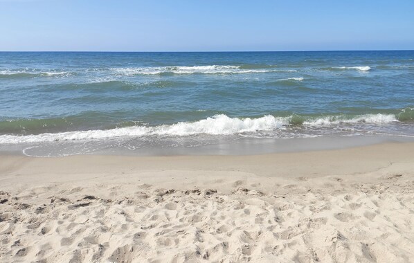 Ein Sandstrand mit sanften Wellen und blauem Himmel.