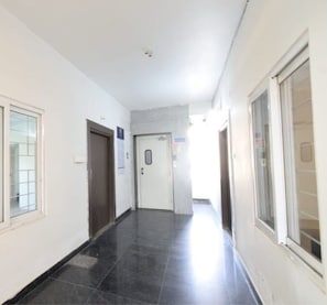 A corridor with white walls, a tiled floor, and doors leading to rooms. - Classic Adithya Stay (Hyderabad)
