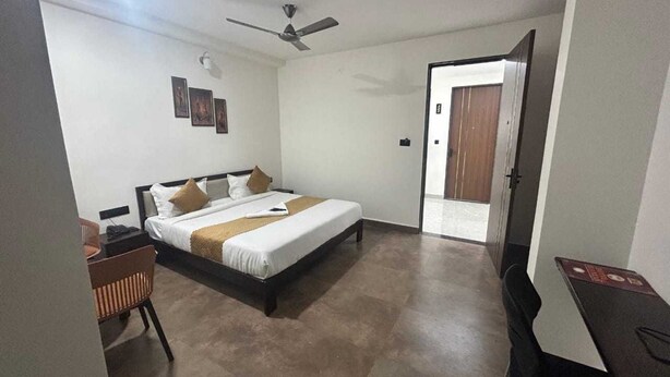 Ein Hotelzimmer mit Bett, Schreibtisch, Stuhl, Deckenventilator und einer Tür zu einem anderen Raum.