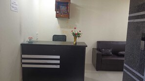 A reception desk with a vase of flowers, a framed picture above it, and a sofa in the background. - Classic Adithya Stay (Hyderabad)