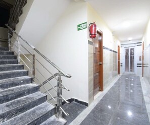 A hotel corridor with marble stairs, a fire exit sign, and a fire extinguisher. - Classic Adithya Stay (Hyderabad)