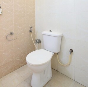 A standard white toilet with a tank, a wall-mounted flush handle, and a visible pipe. - Classic Adithya Stay (Hyderabad)